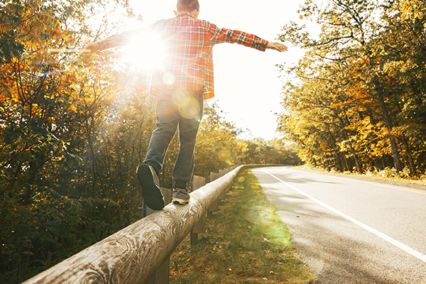 boy walking along the road fence. child keeps balance on the log
